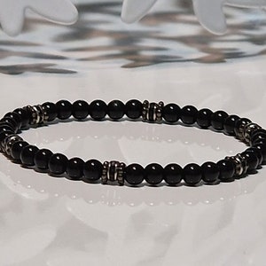 Op de afbeelding: Een zwarte kralen armband met zilveren accenten. De armband is gemaakt van kleine, ronde kralen en heeft een eenvoudig, elegant ontwerp.