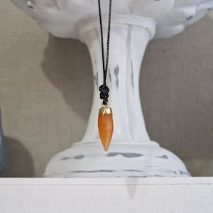 May include: A gold-tipped orange gemstone pendant on a black cord necklace.