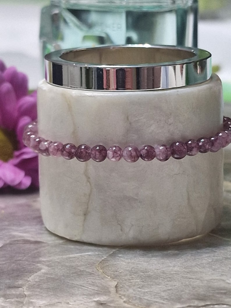 May include: A purple amethyst gemstone bracelet with small round beads. The bracelet is resting on a white marble surface.