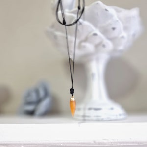 May include: A simple necklace with a black cord and a small, orange, teardrop-shaped pendant.