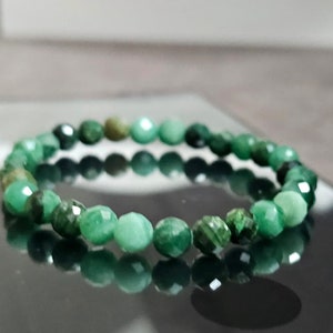 Puede incluir: Un brazalete de piedras preciosas verdes hecho de cuentas facetadas. El brazalete está sobre una superficie negra.