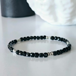May include: A black beaded bracelet with silver accents. The bracelet is made of small, faceted black beads and two silver beads with a decorative design.