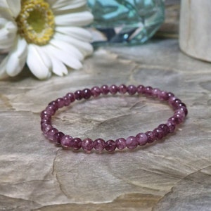 May include: A purple amethyst gemstone bracelet with small round beads. The bracelet is on a textured brown surface.