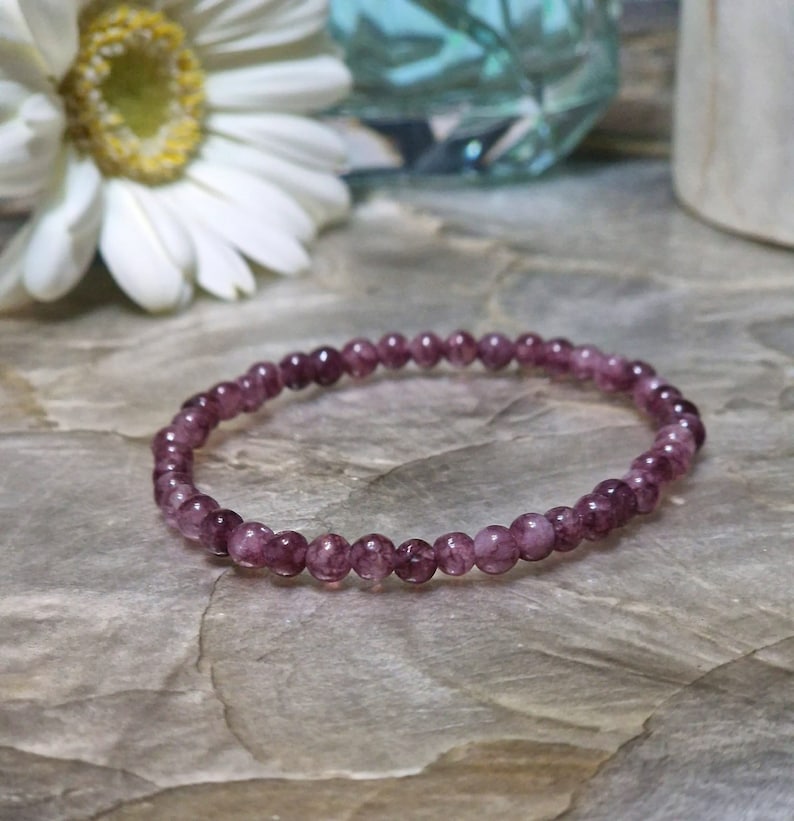 May include: A purple amethyst gemstone bracelet with small round beads. The bracelet is on a textured brown surface.