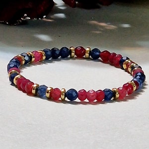 Op de afbeelding: Een rode en blauwe kralen armband met gouden accenten. De armband is gemaakt van kleine, ronde kralen en is geregen op een dunne, gouden ketting.