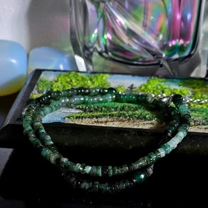 Puede incluir: Un collar de cuentas de piedras preciosas verdes con un cierre de plata. El collar está hecho de pequeñas cuentas redondas que están enhebradas en una fina cadena de plata.