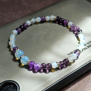 Könnte beinhalten: Ein violettes und weißes Perlenarmband mit silbernen Akzenten. Das Armband besteht aus Amethyst- und Opalperlen.