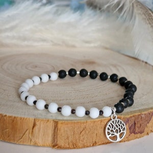 May include: A black and white beaded bracelet with a silver tree of life charm. The bracelet is made with lava rock and white beads.