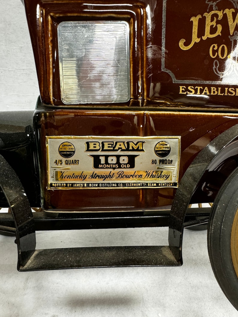 Puede incluir: Una jarra de cer&aacute;mica marr&oacute;n con forma de cami&oacute;n antiguo, con el texto "BEAM" y "Kentucky Straight Bourbon Whiskey". La jarra tiene una ventana plateada y letras doradas. Se lee "4/5 Quart" y "100 Months Old".