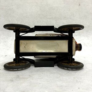 Puede incluir: Una botella de licor de estilo vintage con forma de coche cl&aacute;sico. El marco negro sostiene la botella, con cuatro ruedas y un tap&oacute;n marr&oacute;n. La botella tiene el texto "Creation of James B. Beam".