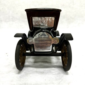 Puede incluir: Un coche de juguete negro vintage con techo marr&oacute;n y ruedas doradas. El coche presenta una parrilla y faros plateados, sobre un fondo blanco. El dise&ntilde;o cl&aacute;sico evoca nostalgia.