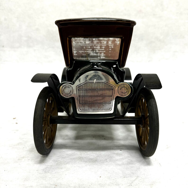 Puede incluir: Un coche de juguete negro vintage con techo marr&oacute;n y ruedas doradas. El coche presenta una parrilla y faros plateados, sobre un fondo blanco. El dise&ntilde;o cl&aacute;sico evoca nostalgia.