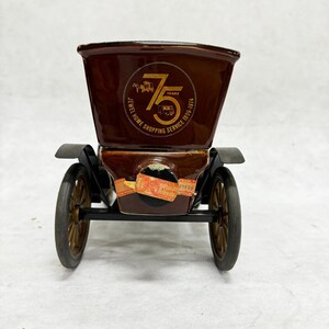 Puede incluir: Un recipiente de cer&aacute;mica marr&oacute;n con forma de coche antiguo con ruedas doradas. El recipiente tiene un logotipo que dice "Jewel Home Shopping Service 75 Years 1899-1974". El coche tiene guardabarros negros y una pegatina en la parte delantera.