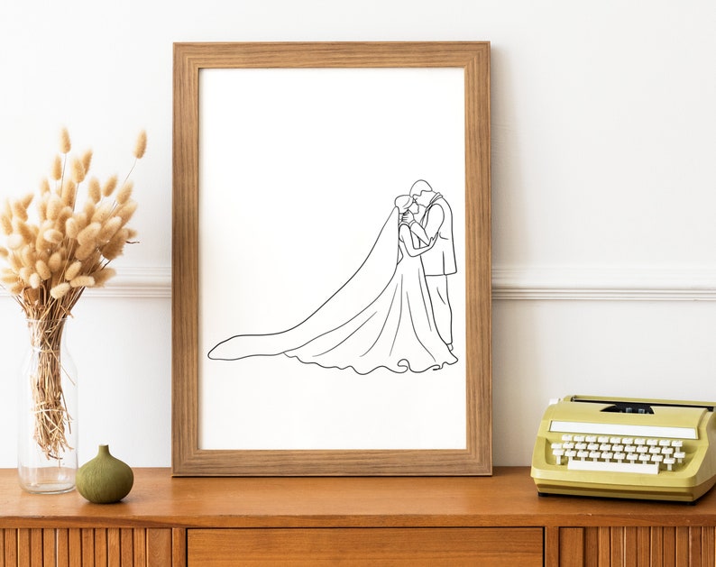 May include: A black and white line drawing of a bride and groom kissing, framed in a light wood frame.