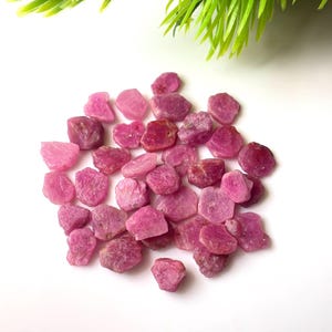 Könnte beinhalten: Eine Ansammlung kleiner, roher, unpolierter Rubin-Edelsteine in verschiedenen Schattierungen von leuchtendem Pink und tiefem Rot. Jeder Stein weist eine unregelmäßige, gezackte Form mit einer natürlichen, matten Textur auf und liegt in einer Gruppe.