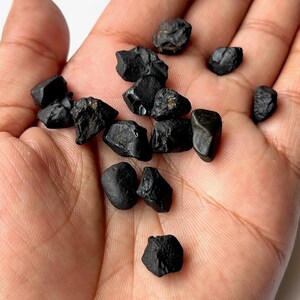May include: A collection of small, black, rough, and irregularly shaped stones. The stones are scattered on a person's hand.