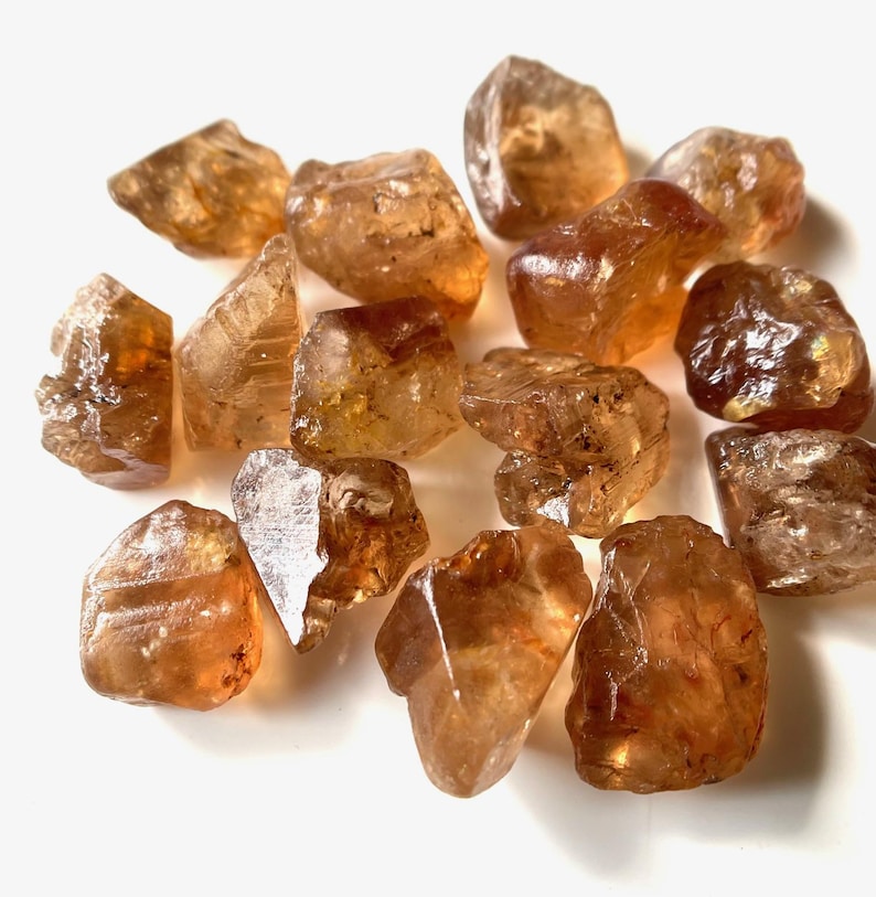 Puede incluir: Una colecci&oacute;n de cristales de citrino en bruto, sin cortar. Los cristales var&iacute;an en tama&ntilde;o y forma, mostrando una gama de tonos &aacute;mbar y marr&oacute;n dorado. Se aprecian la textura rugosa y las formaciones naturales de las piedras.
