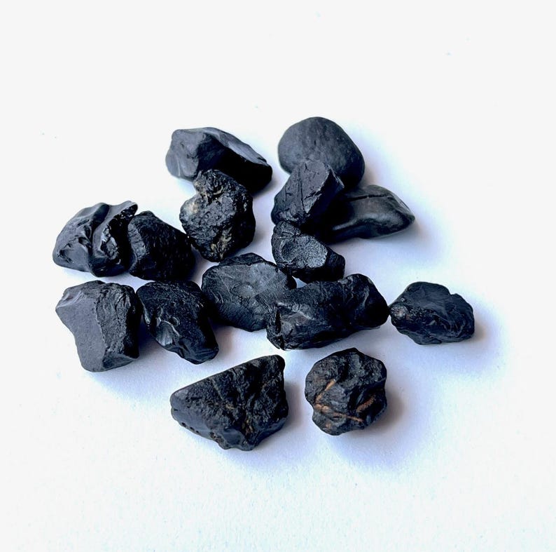 May include: A collection of black obsidian stones, each with a unique shape and texture. The stones are rough and have a natural, unpolished look.