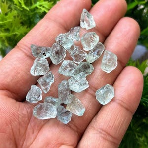 May include: A collection of small, light blue aquamarine crystals in a hand. The crystals are rough and have a natural, unpolished look.