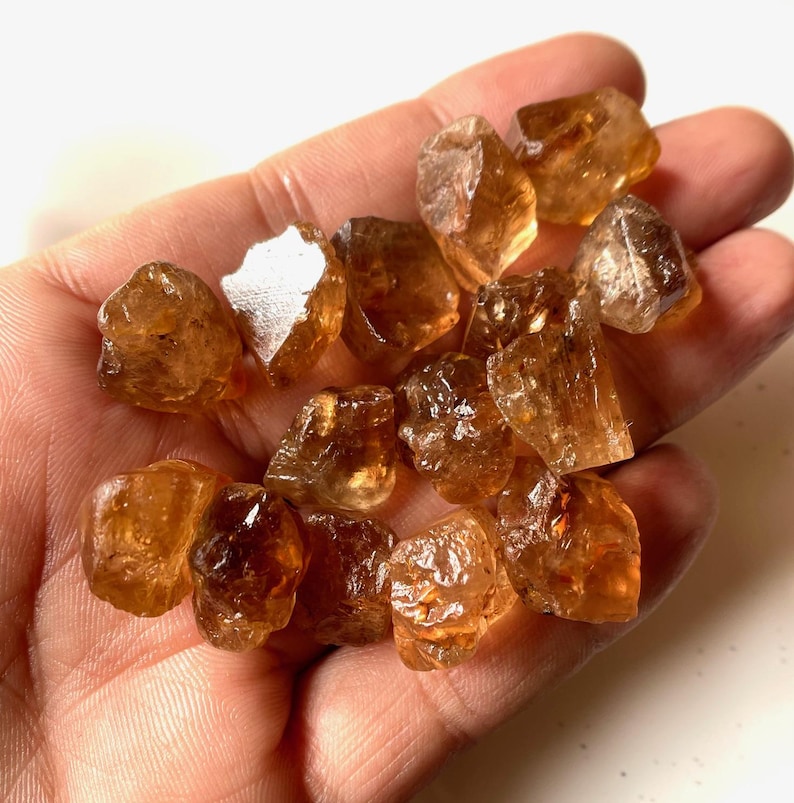 Puede incluir: Un pu&ntilde;ado de cristales de citrino en bruto y sin cortar. Los cristales son de un color &aacute;mbar c&aacute;lido, con una textura natural rugosa. Las piedras preciosas var&iacute;an en tama&ntilde;o y forma, algunas parecen m&aacute;s transl&uacute;cidas. Citrino natural.