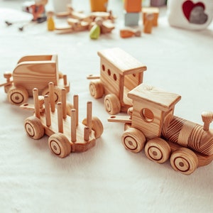 May include: Wooden toy train set featuring a locomotive, a passenger car, and a flatbed car with wooden dowels. The train cars are made of light-colored wood and have round wheels. The set is designed for children.