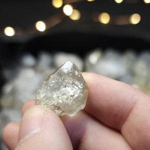 Peut inclure: Un cristal de quartz clair avec une forme pointue et des facettes iris&eacute;es. Le cristal est tenu dans une main.