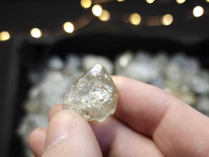 Peut inclure: Un cristal de quartz clair avec une forme pointue et des facettes iris&eacute;es. Le cristal est tenu dans une main.
