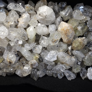 Peut inclure: Une collection de cristaux de quartz transparents de formes et de tailles vari&eacute;es. Les cristaux sont principalement transparents, mais certains ont une l&eacute;g&egrave;re teinte jaune ou brune. Les cristaux sont dispos&eacute;s en tas, et certains se chevauchent.