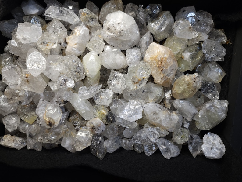 Peut inclure: Une collection de cristaux de quartz transparents de formes et de tailles vari&eacute;es. Les cristaux sont principalement transparents, mais certains ont une l&eacute;g&egrave;re teinte jaune ou brune. Les cristaux sont dispos&eacute;s en tas, et certains se chevauchent.