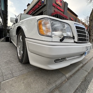 Könnte beinhalten: Ein weißer Mercedes-Benz Kombi, der auf einer Straße mit einem Bürgersteig aus Ziegeln geparkt ist. Das Auto hat eine schwarze Stoßstange und einen schwarzen Kühlergrill. Das Auto hat ein Nummernschild mit der Aufschrift "34 6008".