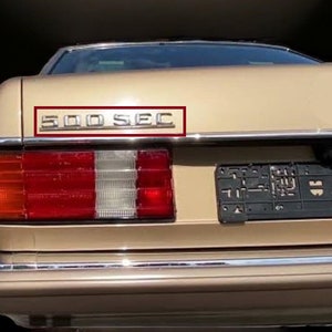 May include: A beige car with a chrome 500 SEC emblem on the back.