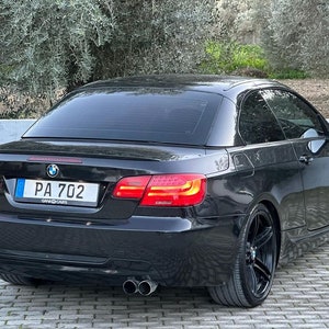 May include: A black BMW 3 Series convertible with a black license plate that reads "PA 702". The car is parked on a brick driveway.