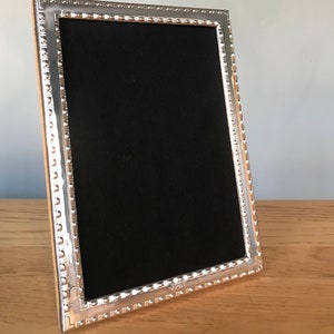 May include: A silver picture frame with a beaded border. The frame is empty and has a black velvet backing.