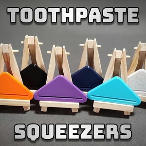 May include: Six different coloured toothpaste squeezers on small wooden easels. The colours are orange, black, purple, navy blue, turquoise, and grey.