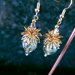 Puede incluir: Pendientes de oro con cuentas de piedra verde y blanca y detalles de flores doradas.