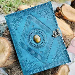 Op de afbeelding: Teal lederen dagboek met ingewikkelde gegraveerde patronen en een decoratieve sluiting. De omslag heeft een grote, ronde tijgeroog steen.