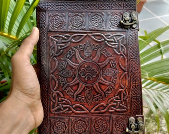 May include: A brown leather journal with a Celtic knot design and a sun motif. The journal has two brass clasps.