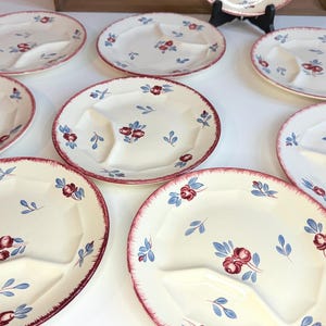 May include: A set of cream-coloured divided plates with a red rim and floral design. The plates have a three-section design and are decorated with red and blue floral patterns. The plates are arranged on a white surface.