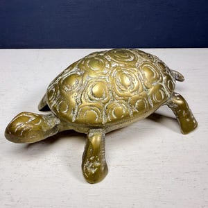 May include: A vintage brass turtle ornament with a detailed shell pattern. The turtle has four legs, a head, and a small tail. The brass has a slightly aged appearance, giving it a classic look. This decorative item is suitable for home decor.