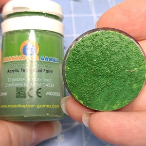 May include: A small bottle of green acrylic paint labelled "Pastoral Green" by Moonhopper Games. The bottle is 20ml and is non-toxic. The paint is designed for technical painting and is suitable for ages 12 and up.
