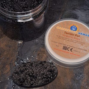 May include: A container of black volcanic rock terrain for model building. The container is labelled "Terrain Pot Volcanic Rock" and "Moonhopper Games".