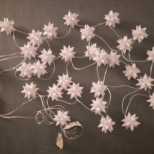 Può includere: Una ghirlanda di luci bianche a forma di stella con un filo bianco. Le luci sono disposte in modo casuale e sono collegate a una spina bianca.