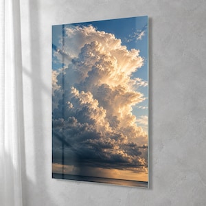 May include: A vertical rectangular wall art piece featuring a high-resolution photograph of a massive, towering cumulonimbus cloud formation against a clear blue sky. The clouds are illuminated by golden sunlight, creating bright highlights and deep shadows.