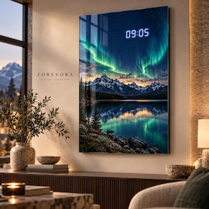 Pode incluir: Um relógio de parede digital de vidro retangular com uma cena de aurora boreal sobre um lago de montanha. A obra mostra picos nevados, pinheiros e margens rochosas refletidas na água. O texto FOREVORA DIGITAL GLASS ART está impresso à esquerda, com um visor digital branco que mostra a hora 09:05 no canto superior direito.