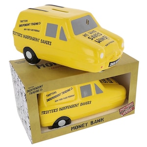 Puede incluir: Huchita de cerámica amarilla con forma de furgoneta con el texto "Trotters Independent Trading Co. New York Paris Peckham" y "Trotters Independent Savers" en el lateral. La furgoneta tiene una rueda blanca y negra y el texto "He who saves wins!" en la parte superior. La huchita está sobre una caja con el texto "Money Bank" y "Only Fools and Horses" en ella.