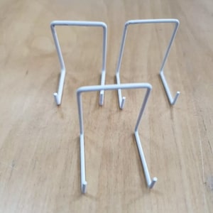 May include: Four white metal display stands for showcasing small items like jewellery or figurines.