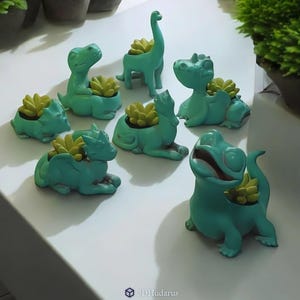 Pode incluir: Uma coleção de vasos em forma de dinossauro em tons de verde-azulado, cada um com uma pequena planta suculenta. Os vasos variam em design, apresentando diferentes espécies de dinossauros. As plantas têm folhas amarelo-esverdeadas. Os vasos estão dispostos sobre uma superfície branca.