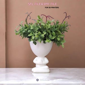 以下が含まれることがあります： 瞑想する人物の形をした白い植木鉢。祈りのために手を合わせ、緑の葉で満たされています。「STL FILE & 3MF FILE FOR 3D PRINTERS」の文字があります。