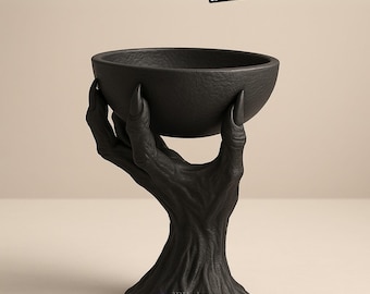 May include: A black bowl held by a sculpted hand, with long fingernails. The bowl and hand are textured and appear to be made of a dark material. The text "Creepy Hand Bowl" is at the top, and "3D Models" is below it.