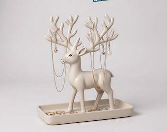 May include: A cream-colored deer jewelry stand with antlers designed to hold necklaces and earrings. The stand has a rectangular base for rings and small jewelry items. The text "DEER JEWELRY STAND" is at the top.